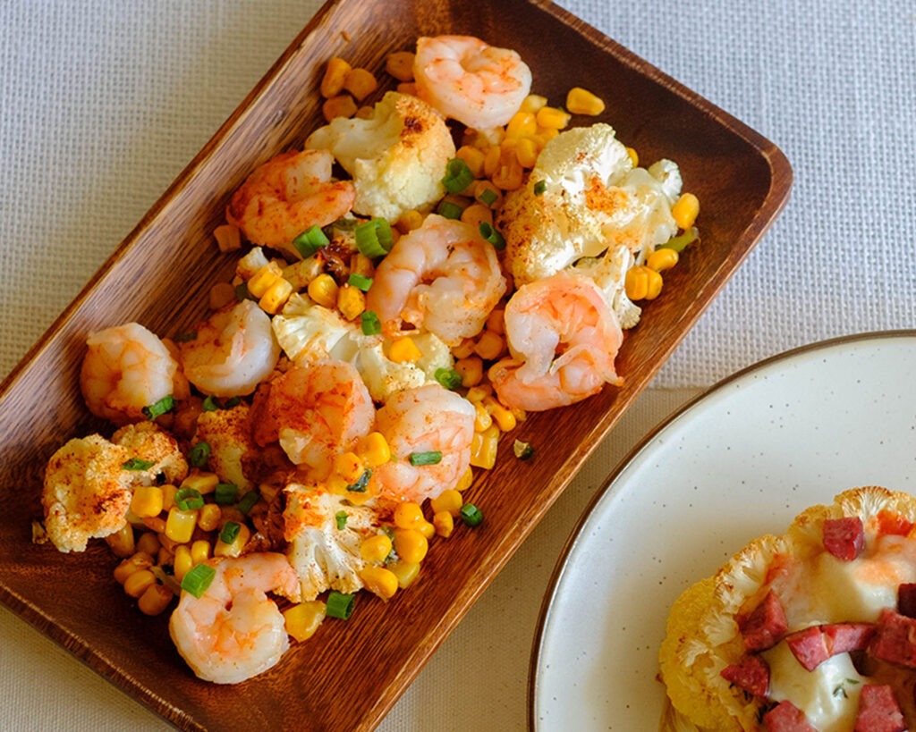 Wood plate with roasted shrimp, corn, cauliflower, and green onions.