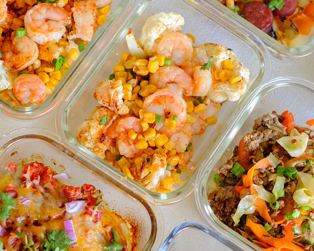 Glass meal prep containers with roasted shrimp, corn, cauliflower, and green onions.