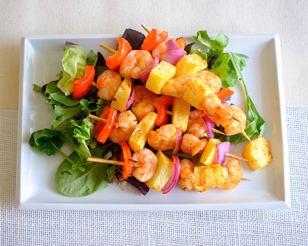 Plate with colorful shrimp kebabs that include shrimp, pineapple, red onions, and red bell pepper.