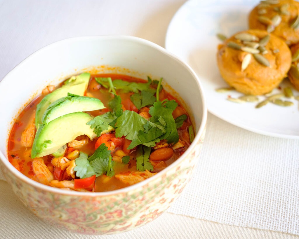 Round bowl of chicken soup with beans, vegetables, avocado, and cilantro