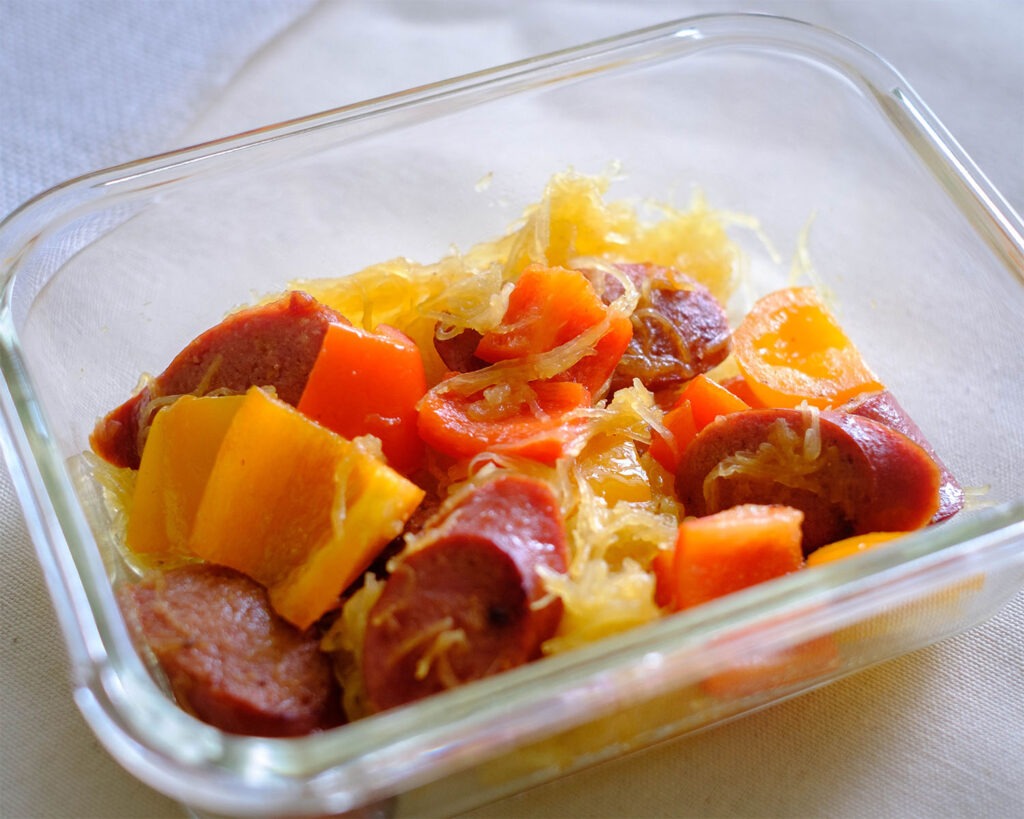 Glass meal prep container with spaghetti squash, sausage, and bell peppers.