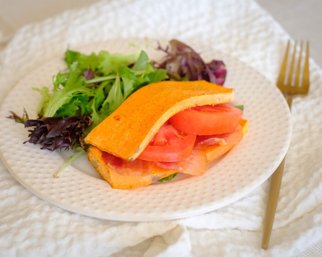 Round plate with sweet potato slices with bacon, tomato, and salad mix.