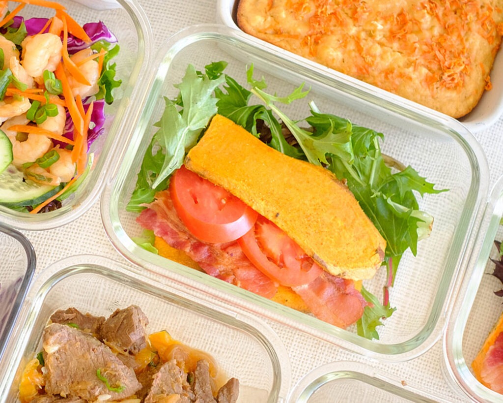 Glass meal prep container with sweet potato slices with bacon, tomato, and salad mix.