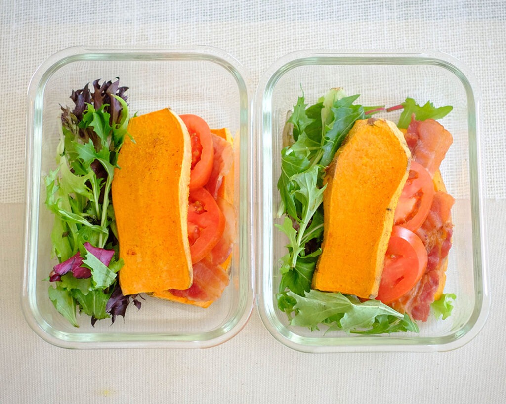 Glass meal prep containers with sweet potato slices with bacon, tomato, and salad mix.