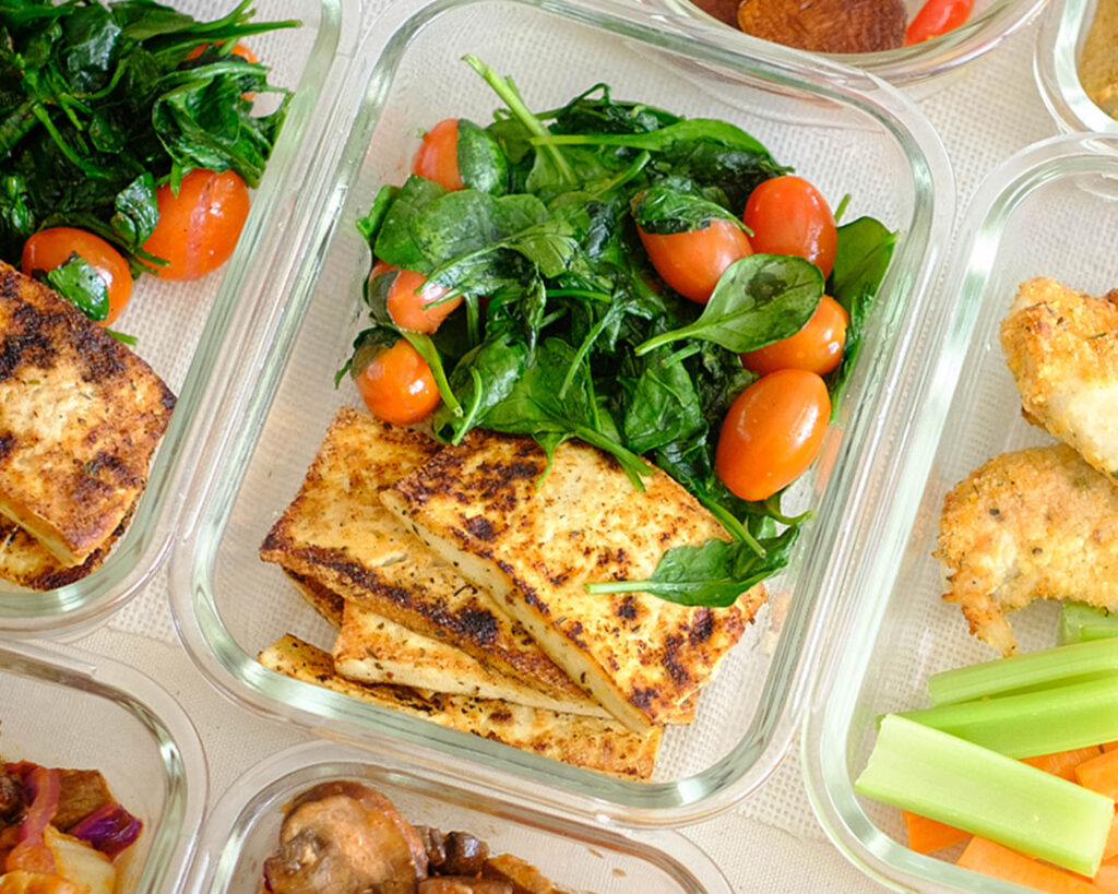 Glass meal prep containers with easy recipe pan-fried tofu topped with sauteed spinach and cherry tomatoes.