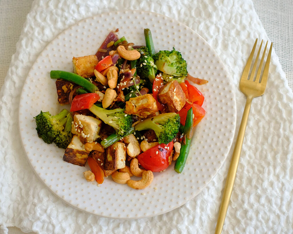 Round plate with tofu stir fry with broccoli, red bell peppers, and cashew nuts.