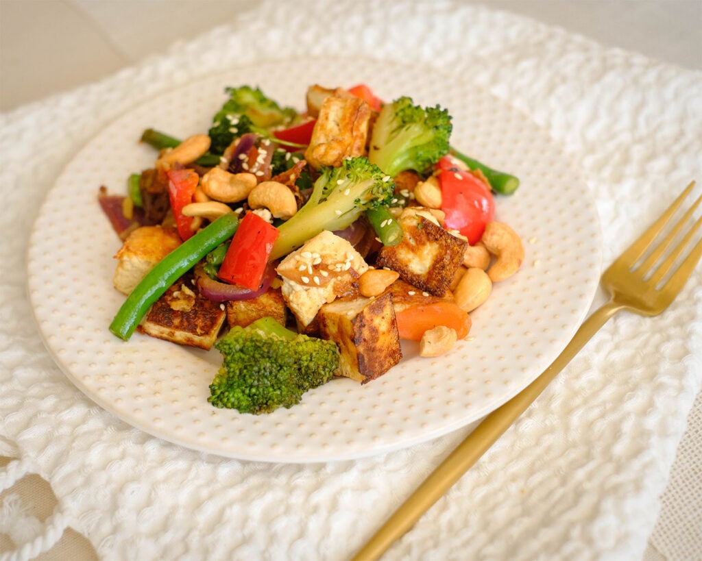 Round plate with tofu stir fry with broccoli, red bell peppers, and cashew nuts.
