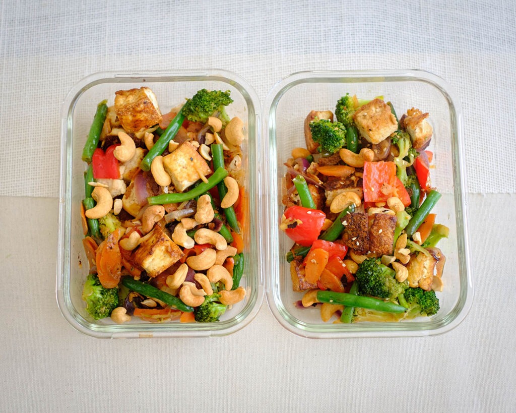 Glass meal prep container with tofu stir fry with broccoli, red bell peppers, and cashew nuts.