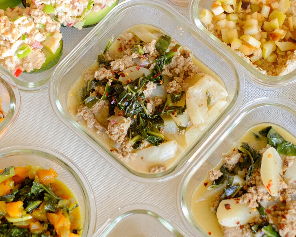 Glass meal prep container with turkey toscana soup that includes ground turkey, potatoes, and leafy greens.
