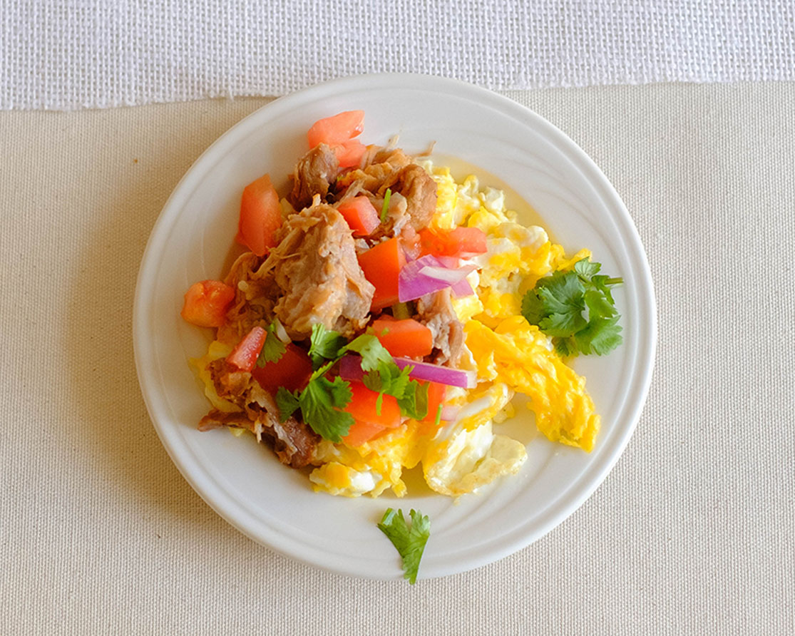 Plate with scrambled eggs topped with pork carnitas and pico de gallo
