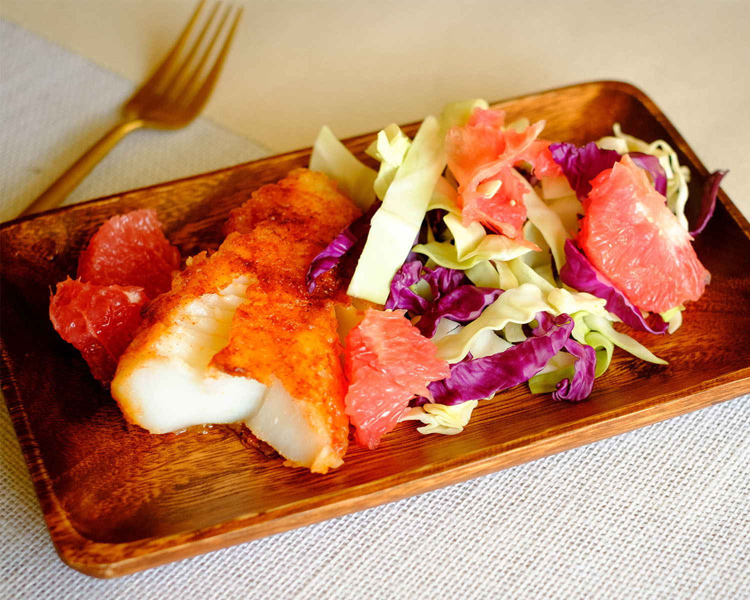 wooden plate with golden brown pan-fried cod filet and grapefruit cabbage slaw.