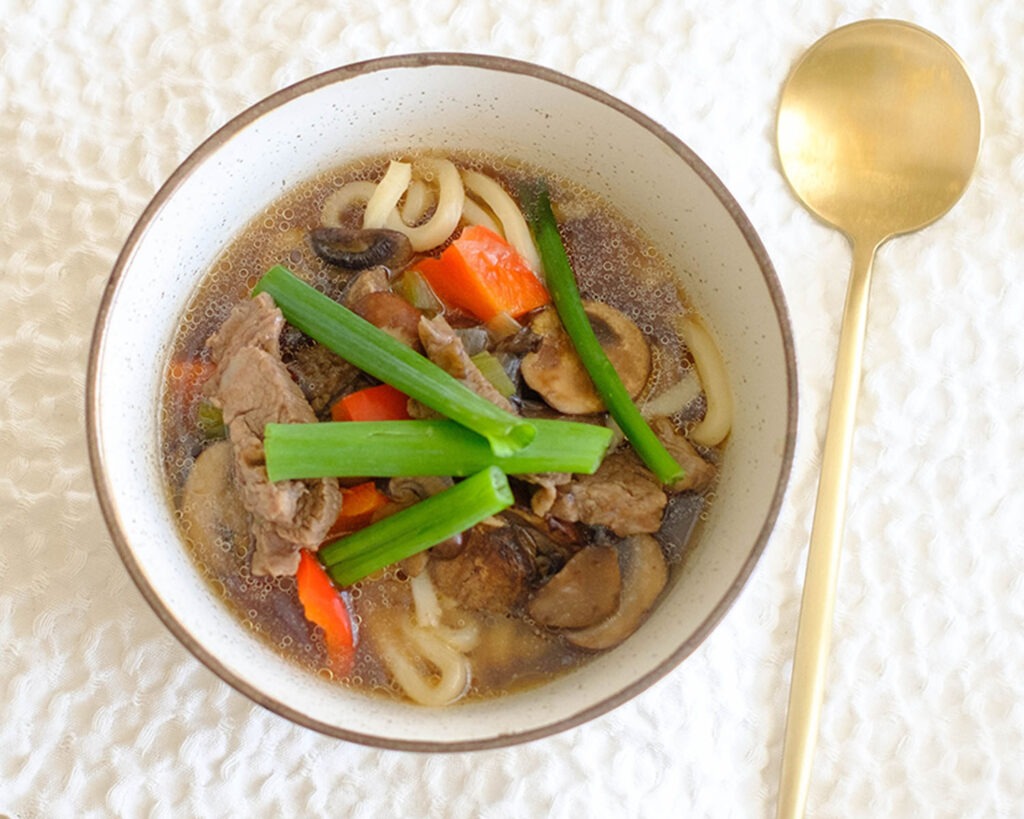 Round bowl with beef soup and udon noodles.