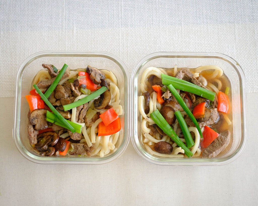 Glass meal prep containers with beef soup and udon noodles.