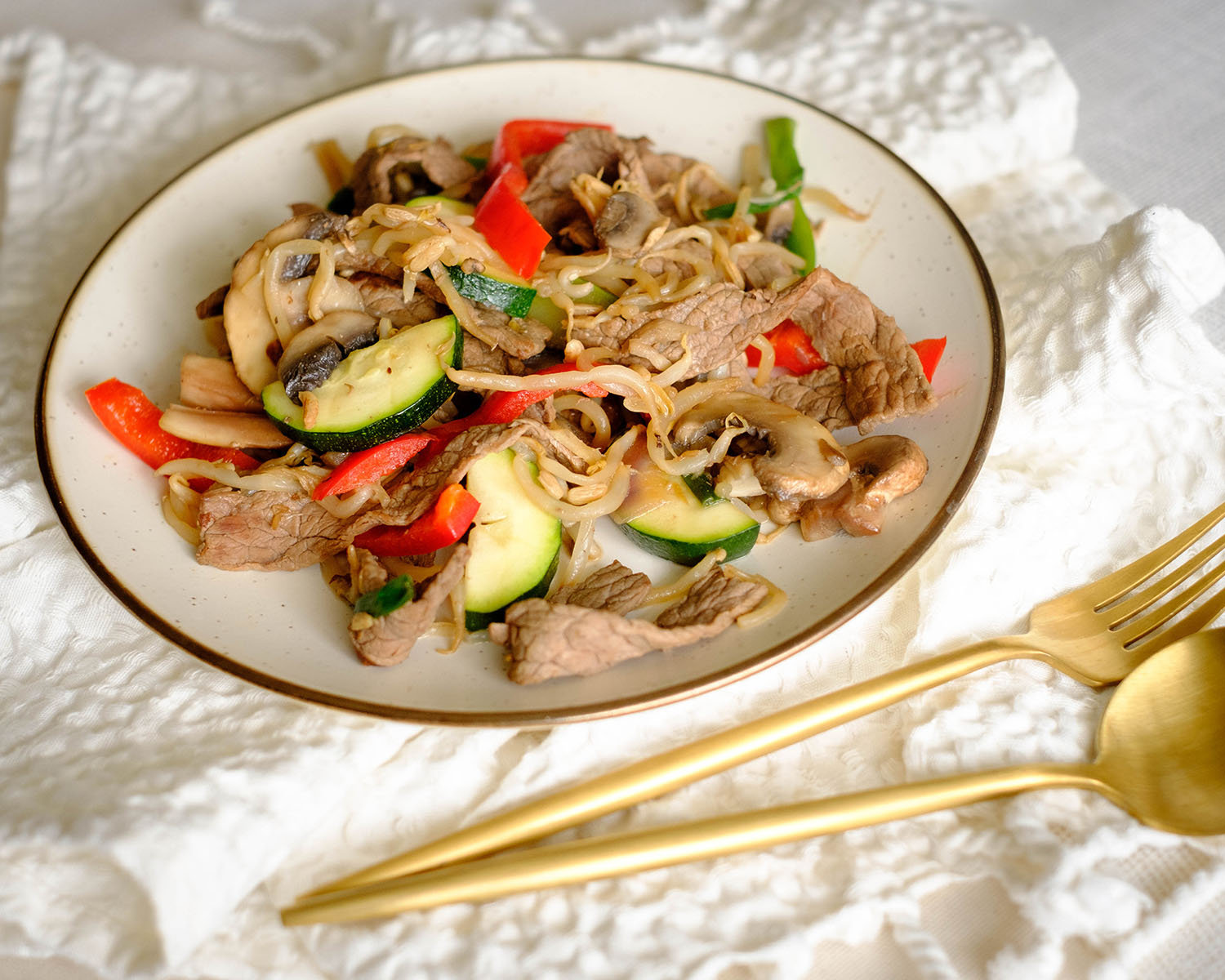 round plate with thin slice beef stir fry with red bell pepper, zucchini, and bean sprouts