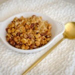 round plate granola, dates, and walnuts on a white cloth with a gold spoon