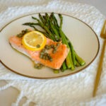 glass meal prep containers with salmon, asparagus, topped with lemon slice and capers