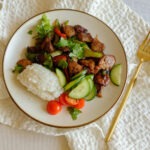 round plate with hoisin pork stir fry with rice, cucumbers and cherry tomatoes