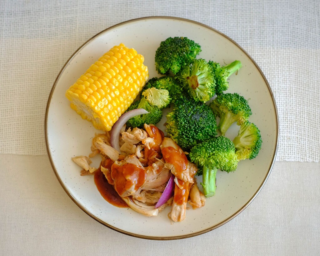 Round plate with shredded instant pot bbq chicken, corn, and broccoli