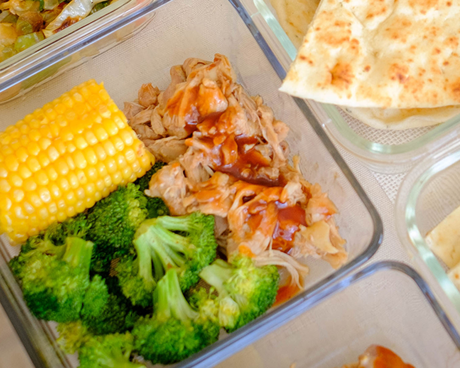 glass meal prep container with shredded bbq chicken, corn, and broccoli