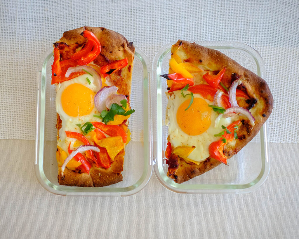glass meal prep container with breakfast pizza with egg, naan bread, and vegetables