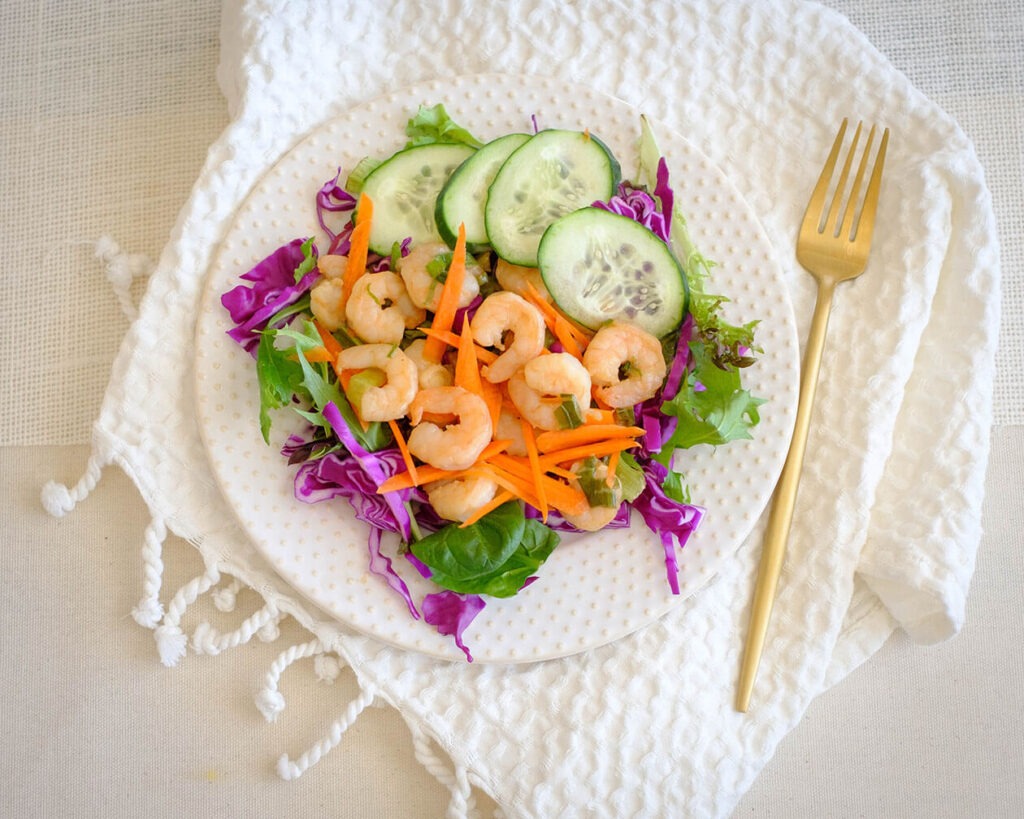 round plate with shrimp salad, and cucumbers, and carrots, and purple cabbage