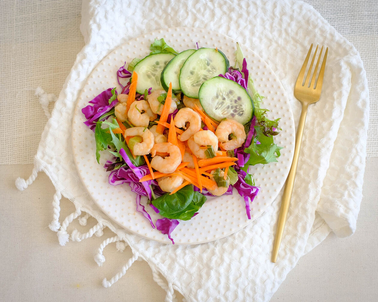 round plate with salad, shrimp, and cucumbers, and carrots, and purple cabbage