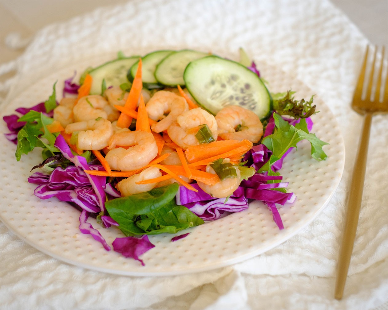 round plate with salad, shrimp, and cucumbers, and carrots, and purple cabbage
