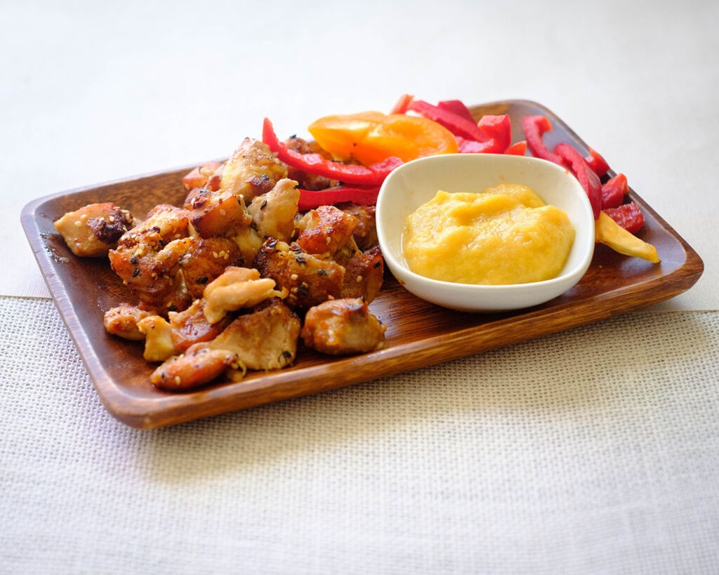 rectangular wooden plate with air fryer chicken recipe - small bite size chicken pieces, sliced red bell peppers, and honey mustard applesauce