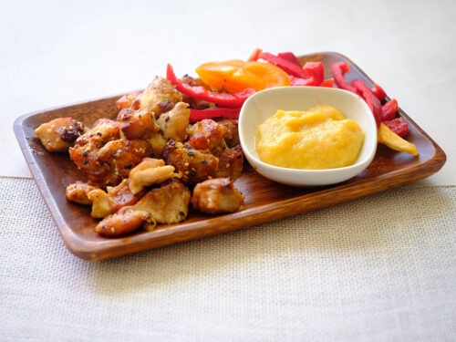 rectangular wooden plate with small bite size chicken pieces, sliced red bell peppers, and honey mustard applesauce