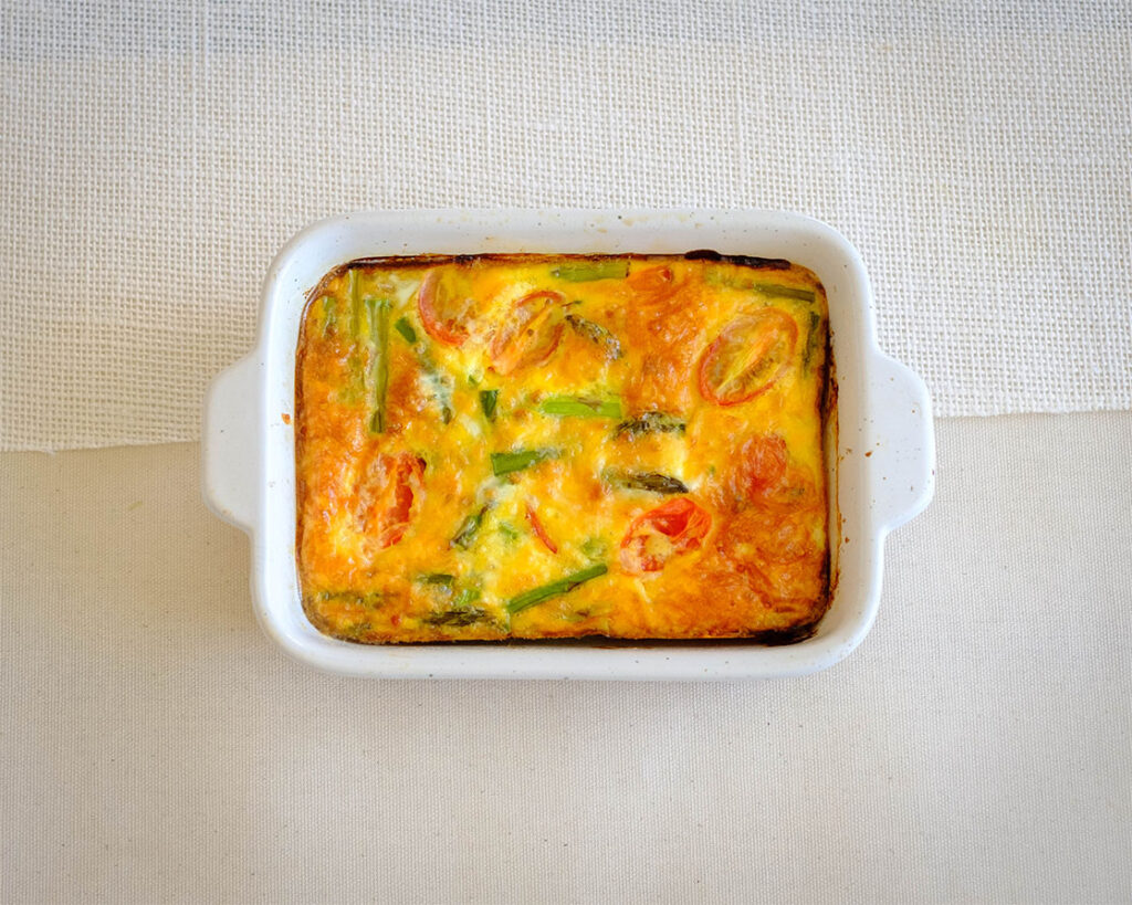 white rectangular baking dish with asparagus and tomato egg frittata