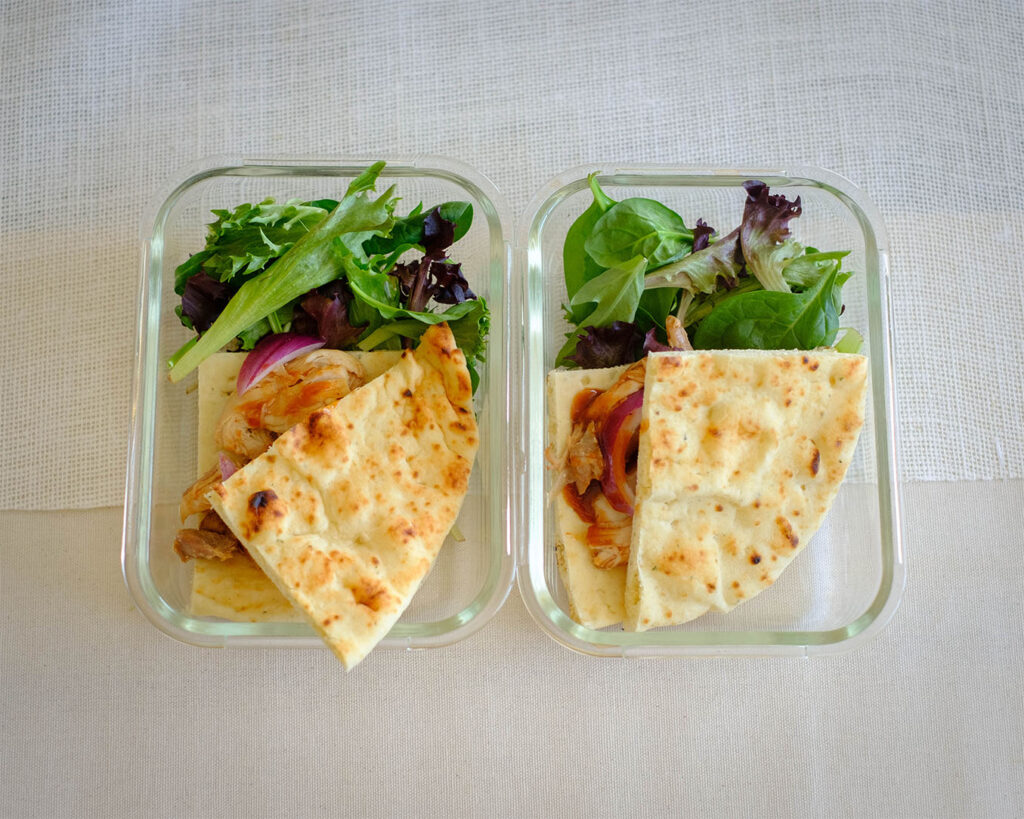 glass meal prep containers with salad and flatbread bbq chicken sandwich