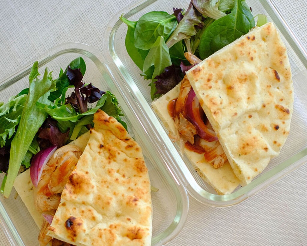 glass meal prep containers with salad and flatbread bbq chicken sandwich