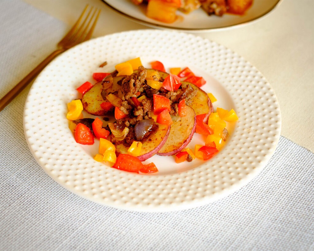 round plate with sliced potatoes rounds, ground beef, and diced bell peppers