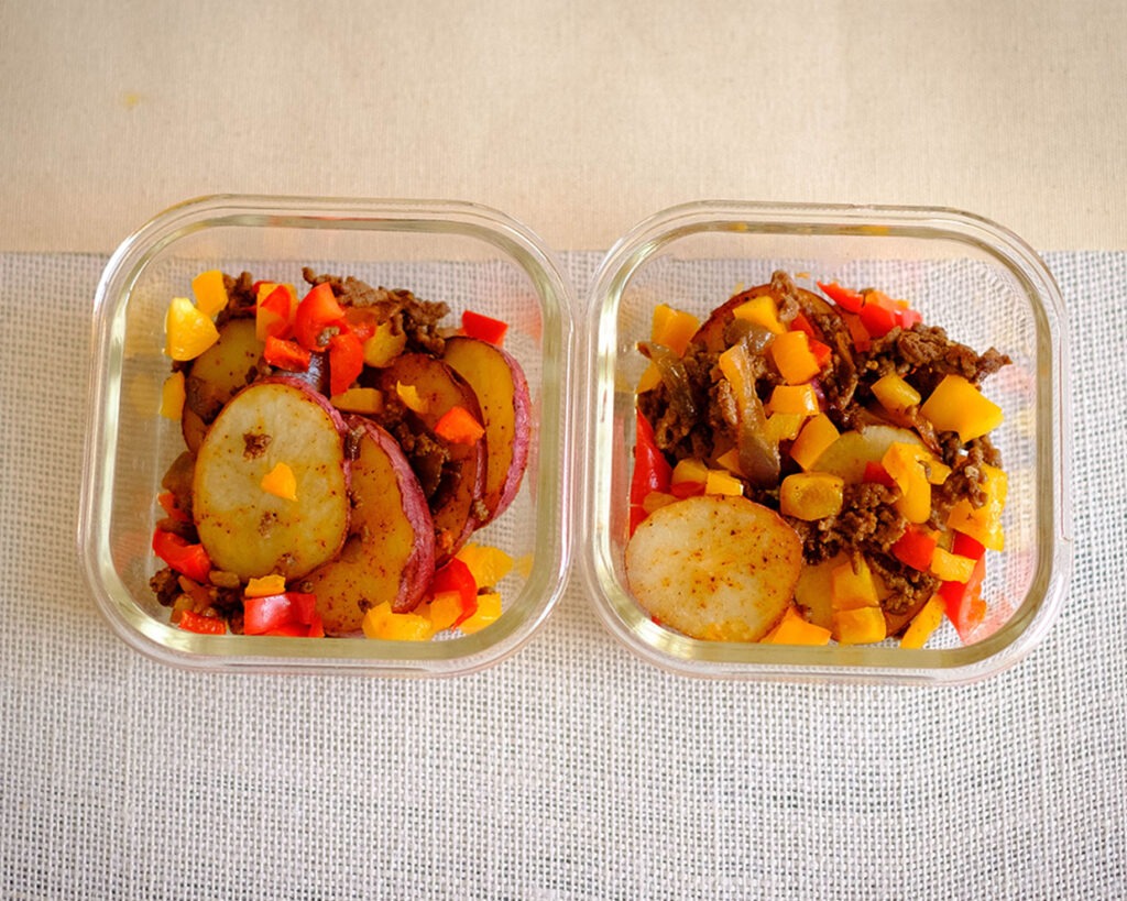rectangle glass meal prep containers with sliced potatoes rounds, ground beef, and diced bell peppers