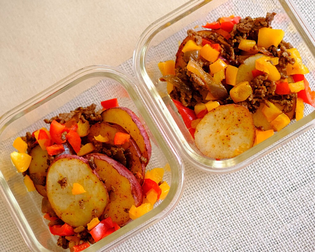 rectangle glass meal prep containers with sliced potatoes rounds, ground beef, and diced bell peppers