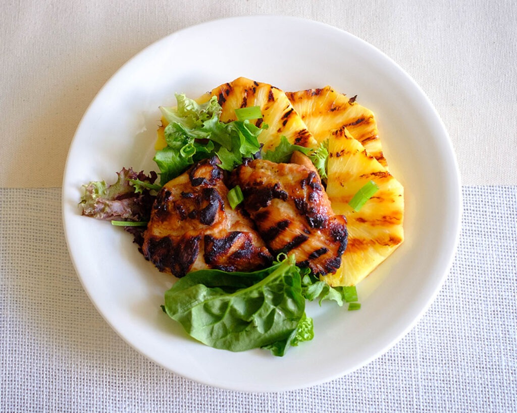 round plate with grilled chicken with grilled pineapple and crisp greens