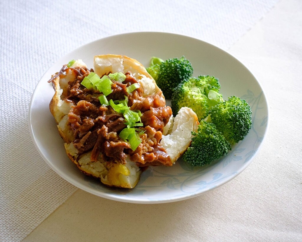 plate with baked potato and instant pot beef bbq on top with broccoli side
