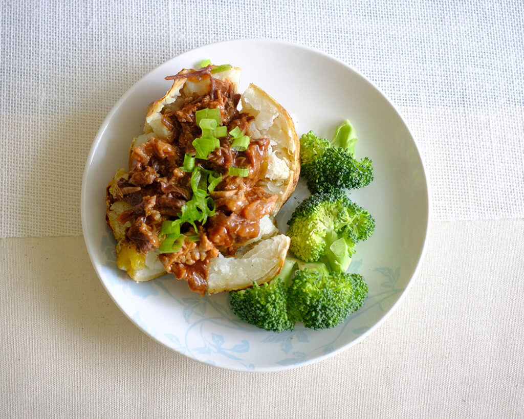 plate with baked potato and instant pot beef bbq on top with broccoli side