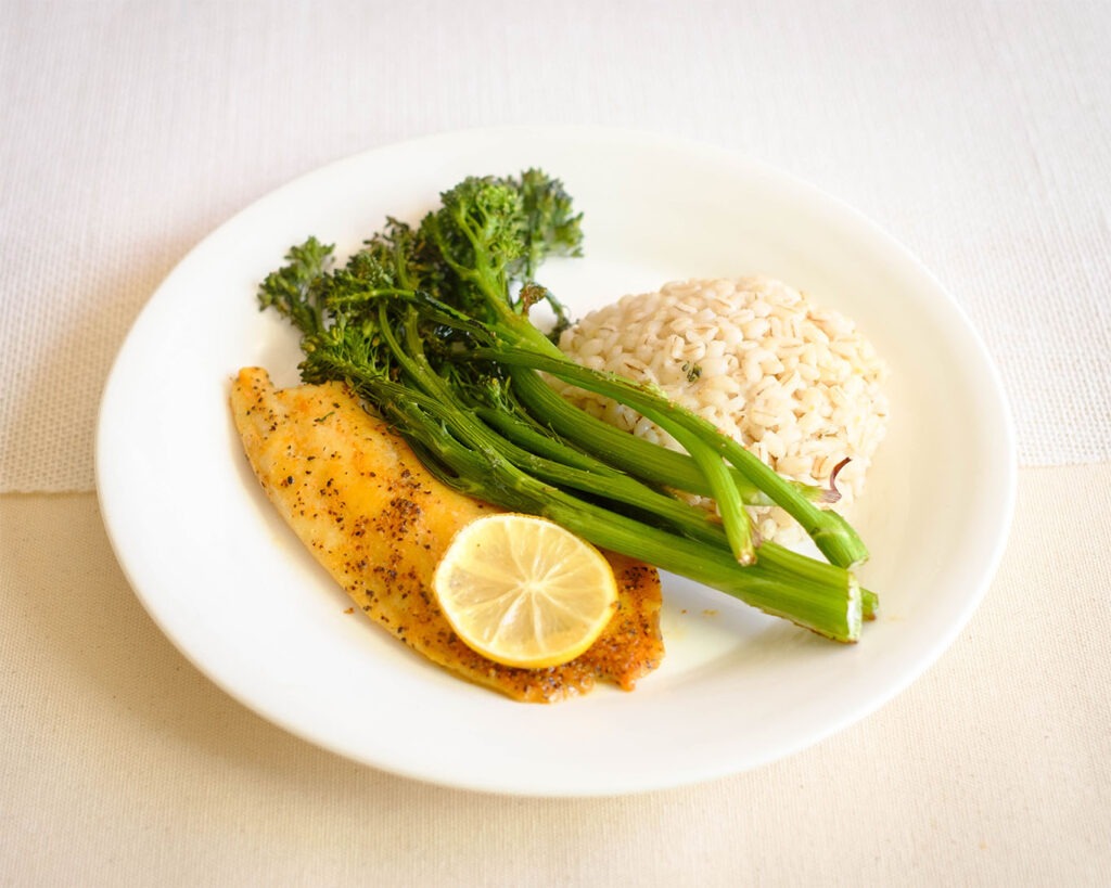 round plate with tilapia fillet, broccolini, and barley - tilapia recipe on plate