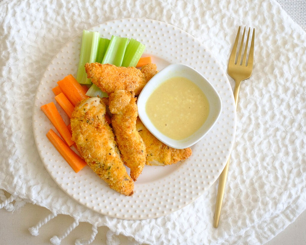 round plate with panko breaded oven baked chicken tenders and carrots and celery and honey mustard