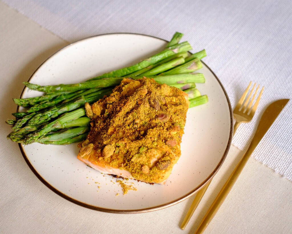 Baked Pistachio Crusted Salmon and Asparagus on a plate with fork and knife next to it
