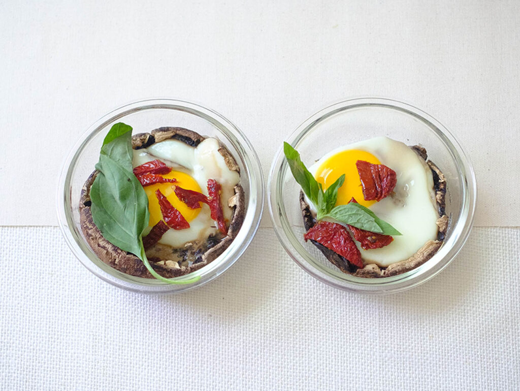 round glass prep bowls with portobello mushroom baked with a egg and topped with sun-dried tomato slices and fresh basil.
