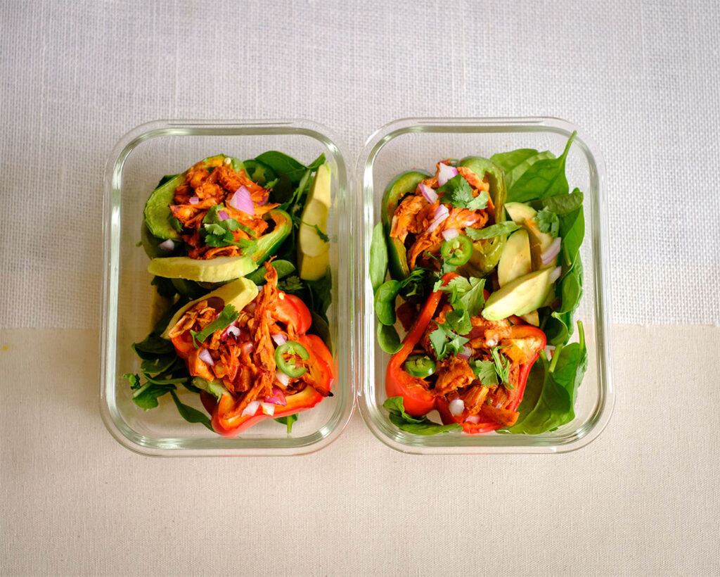 Glass meal prep containers with stuffed peppers with shredded chicken in enchilada sauce.