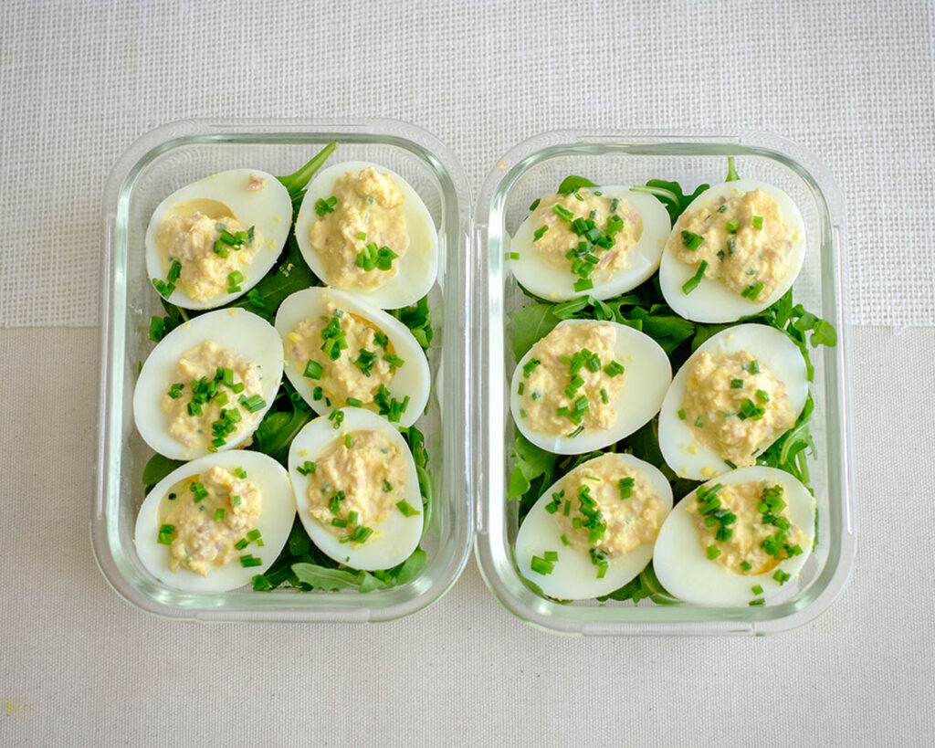 glass meal prep containers with deviled eggs and arugula salad for a low carb meal