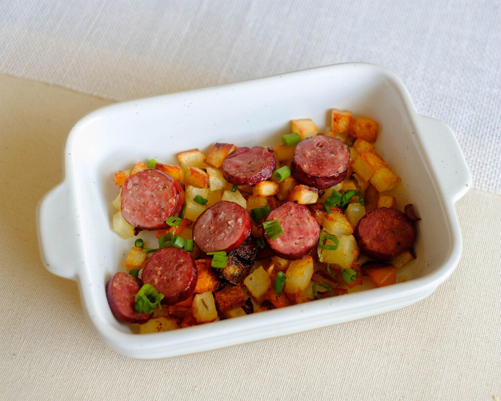 rectangle white baking dish with sliced baked sausage and potato hash diced and peppers, and green onions