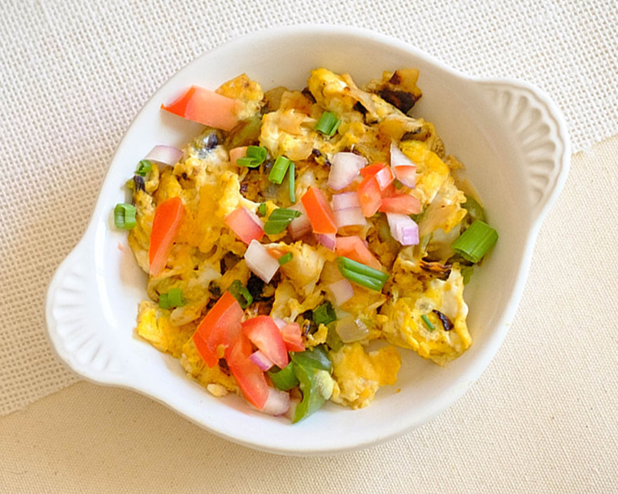 round white plate with scrambled eggs, tomatoes, onions, green onions, and turkey sausage