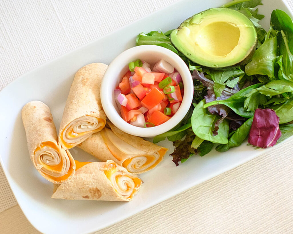 rectangular plate with turkey and cheese air fryer lunch taquitos with pico de gallo, avocado, and spring mix