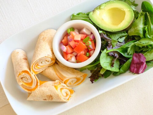 rectangular plate with turkey and cheese taquitos with pico de gallo, avocado, and spring mix