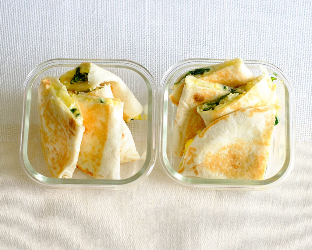 square glass meal prep containers with spinach and egg quesadilla