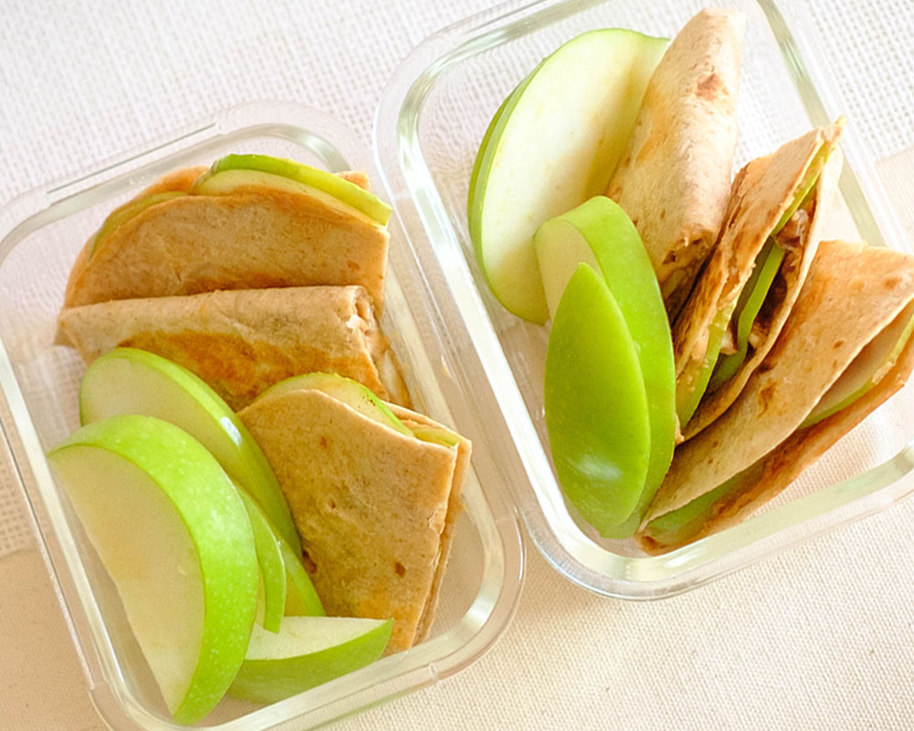 glass meal prep containers with peanut butter quesadillas and sliced green apples